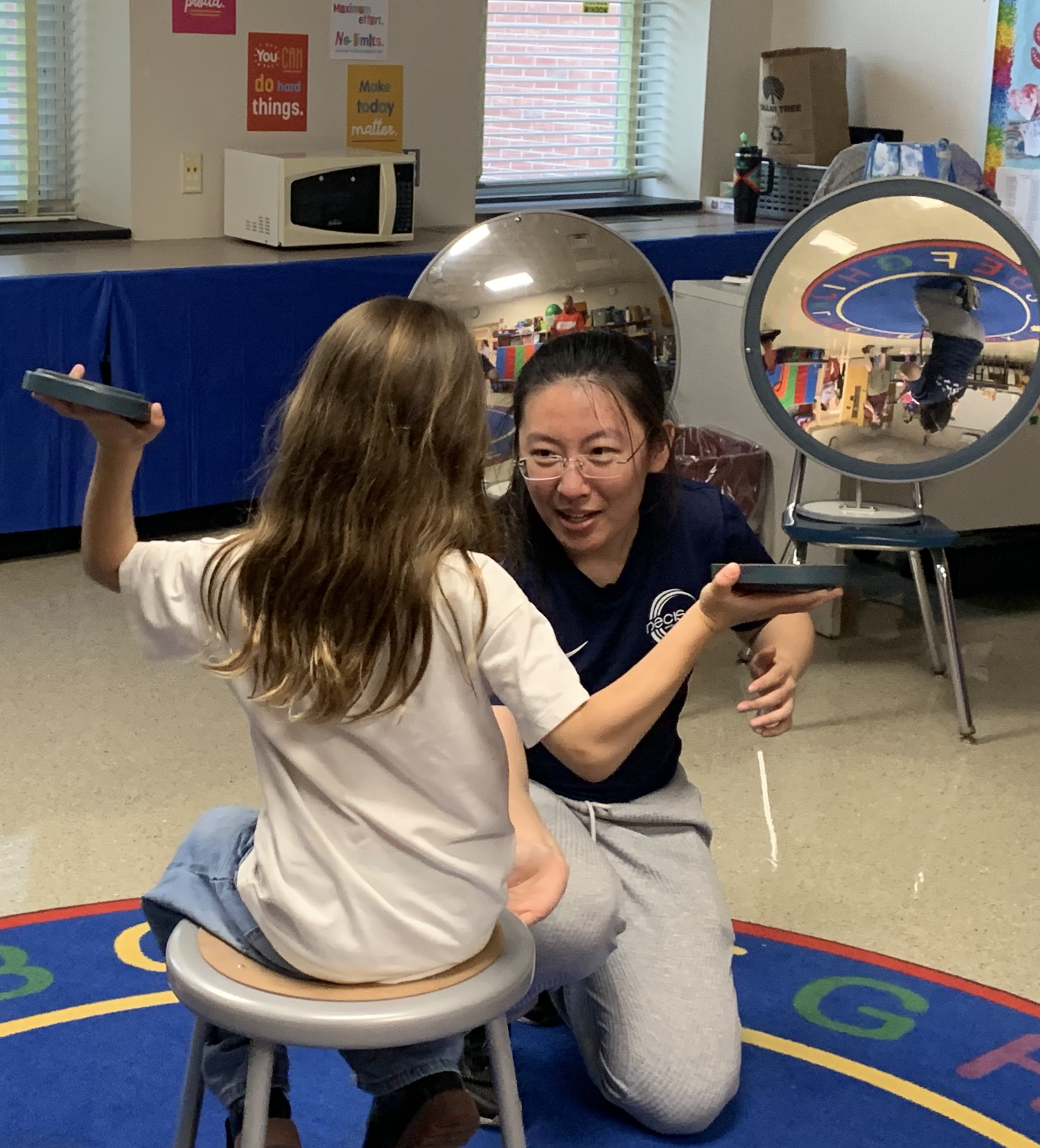 Family STEM night at Leary Elementary school. A child sits on a rotating stool as a volunteer assists.